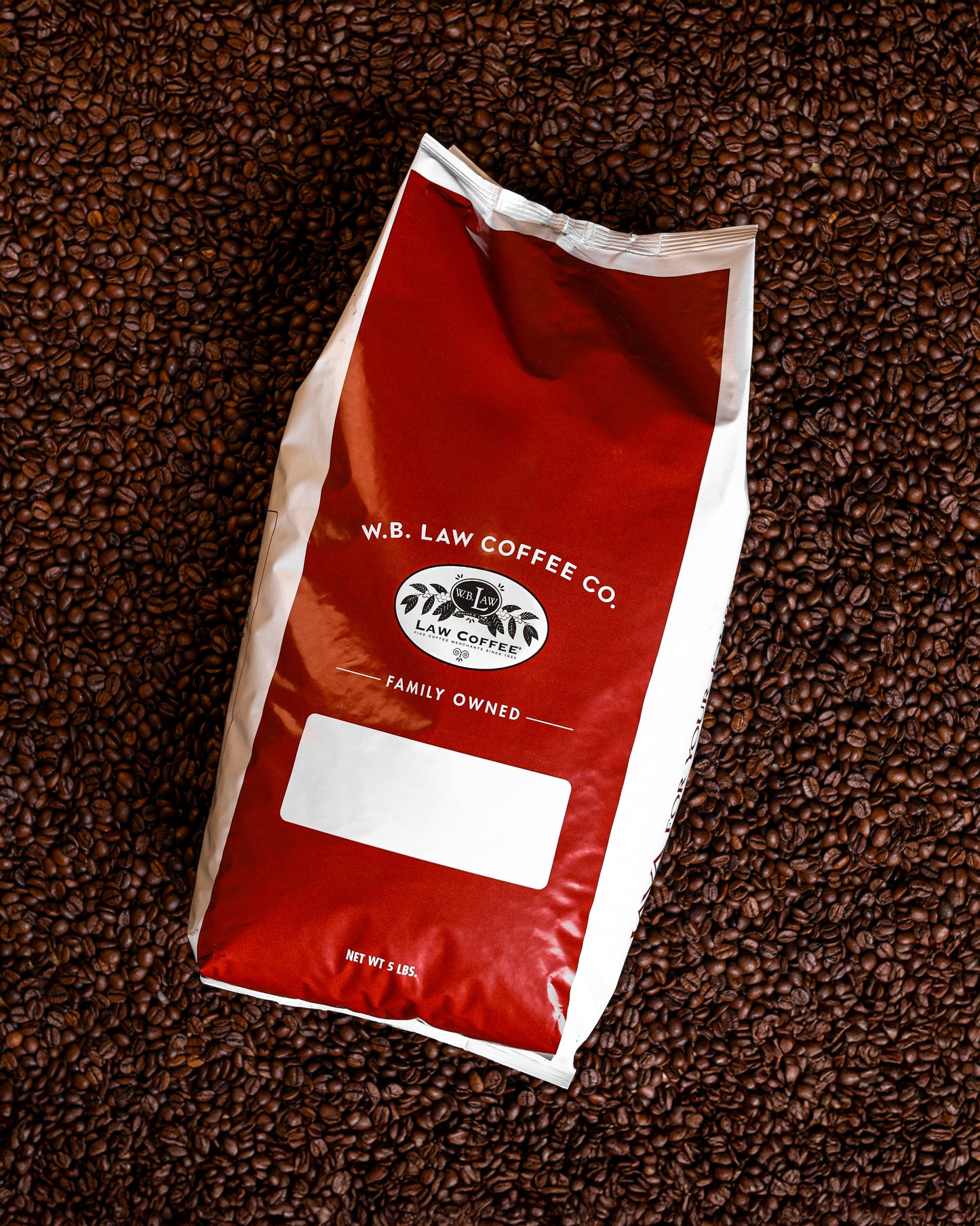A 5lb red and white bag of WB Law Coffee whole bean coffee on a pile of coffee beans.