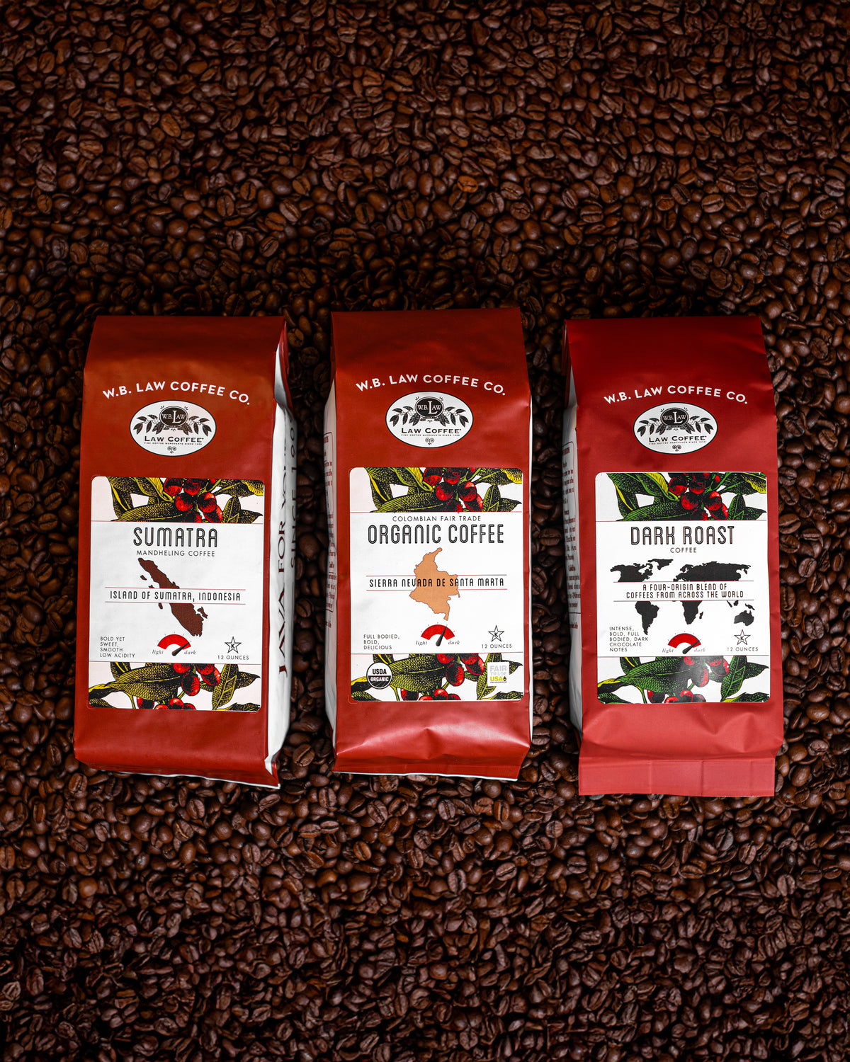 Three bags of dark roasted WB Law Coffees displayed on a background of coffee beans. Each bag has a red label with white text indicating the type of coffee, such as 'Sumatra, Dark Roast, and Organic Colombian Coffee'.