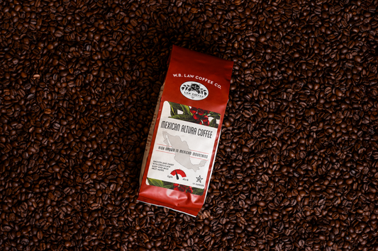 A bag of W.B. Law Coffee Co. Mexican Altura Coffee lies on a dense bed of dark brown coffee beans.