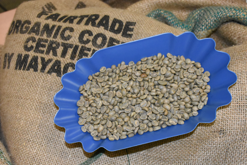 A tray of organic green coffee beans sitting on a burlap sack.