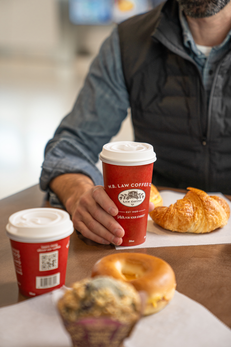 Two WB Law Coffee Cups of coffee next to a croissant, a bagel and a blueberry muffin.