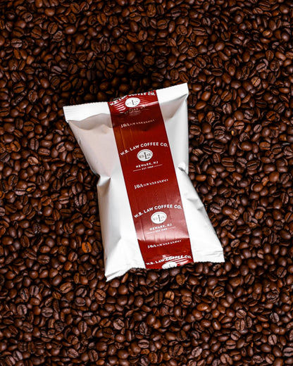 A 2.75oz packaged bag of Law Coffee's Premium House Blend ground coffee, placed on a background of whole coffee beans.