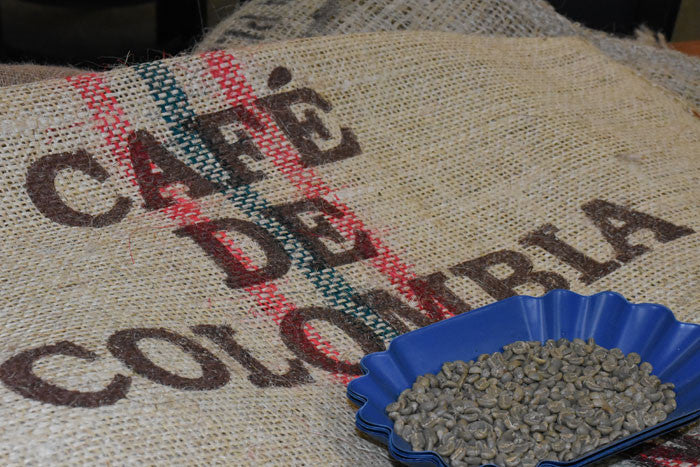 a tray green colombian coffee on a burlap sack that says Cafe de Colombia